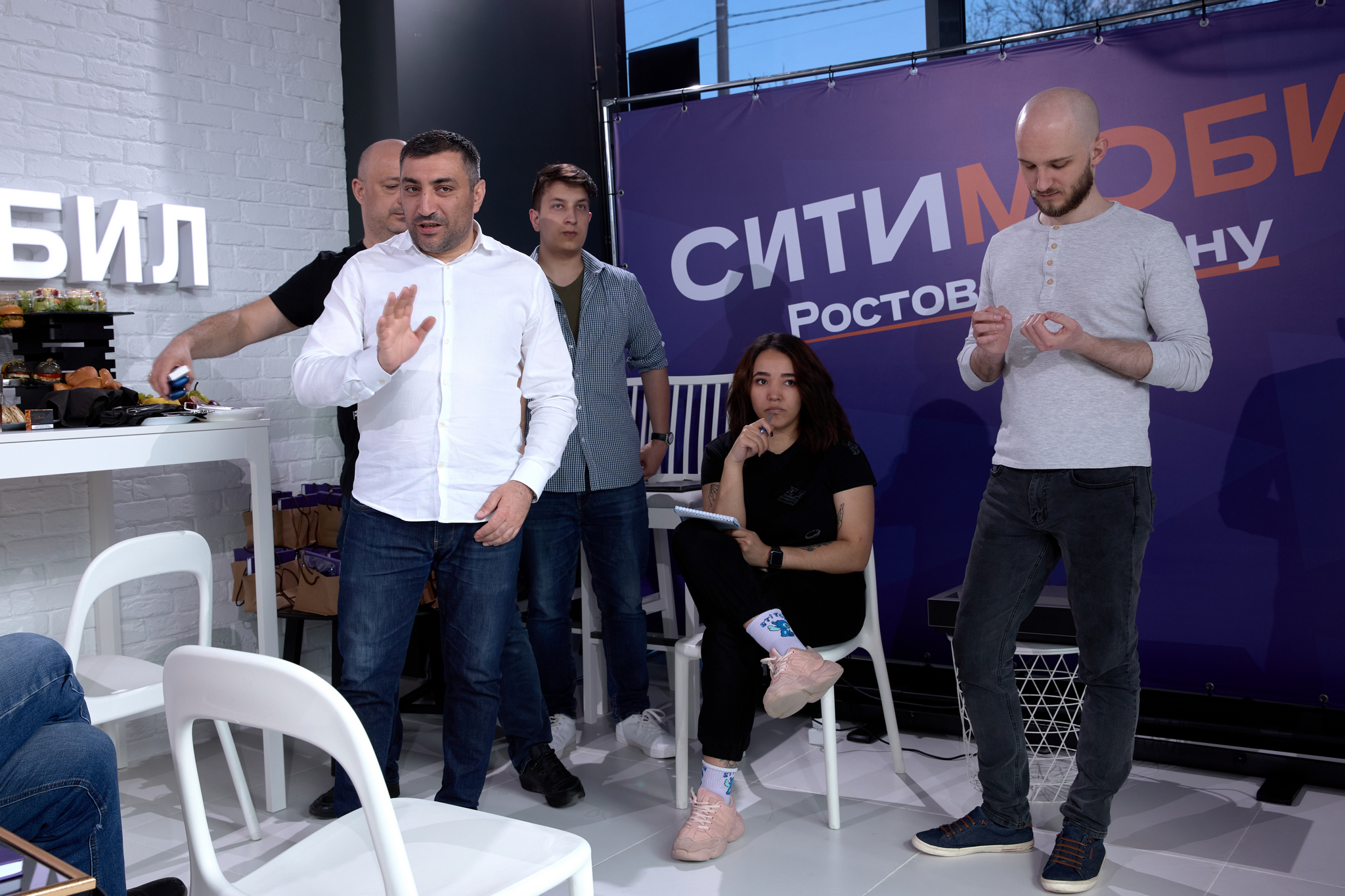 На изображении пять человек: четверо мужчин и одна женщина. Они находятся в помещении с белыми стенами и мебелью. На заднем плане фиолетовый баннер с надписью «Сити-Мобил Ростов».