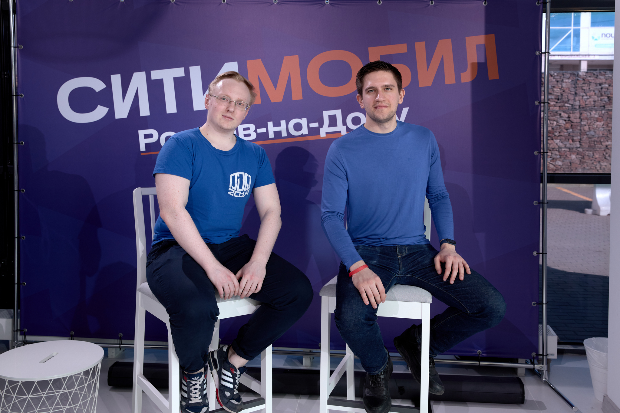 На изображении двое мужчин в синих футболках сидят на белых табуретах перед фиолетовым фоном с надписью «Ситилинк Ростов-на-Дону».